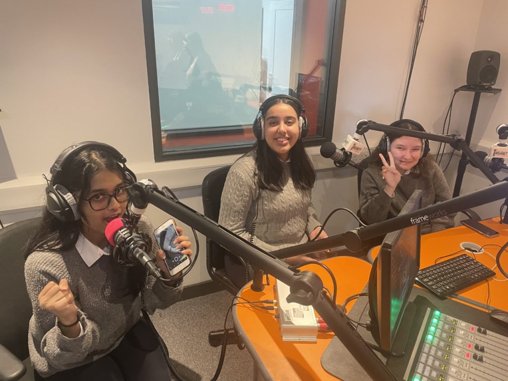 Three female students from the Logic Studio School sit around the Insanity mixing desk. They each wear grey jumpers and black headphones. The mixing desk is a bright orange.